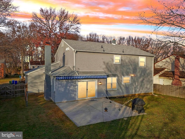 back house at dusk with a patio area and a lawn