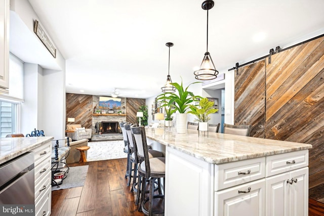 kitchen featuring wooden walls, a barn door, a fireplace, white cabinetry, and a breakfast bar area