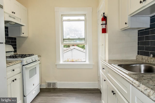 kitchen with white gas stove, tasteful backsplash, light stone counters, hardwood / wood-style floors, and white cabinets