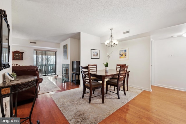 dining space with a fireplace, hardwood / wood-style floors, a textured ceiling, and a notable chandelier