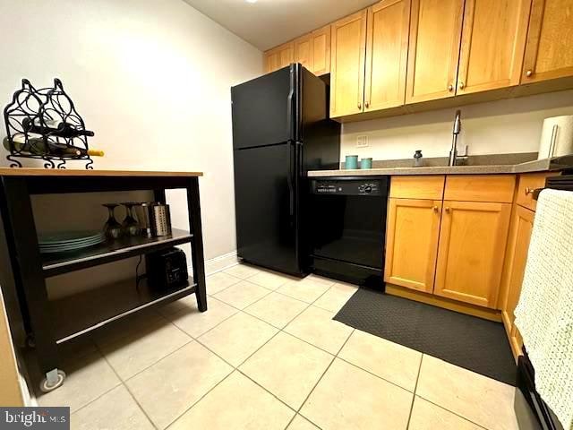 kitchen with light tile patterned floors, brown cabinetry, dark countertops, black appliances, and a sink