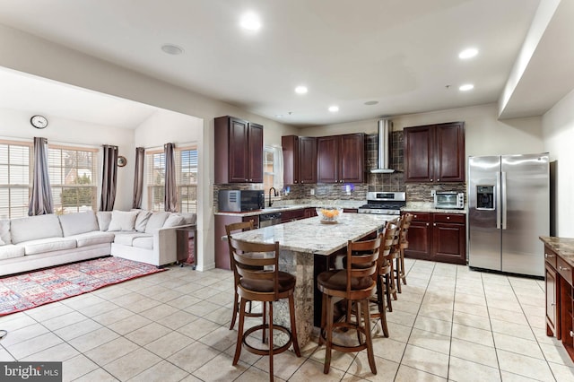 kitchen featuring wall chimney range hood, sink, appliances with stainless steel finishes, tasteful backsplash, and a kitchen island