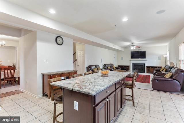 kitchen featuring a kitchen breakfast bar, a kitchen island, dark brown cabinets, and ceiling fan with notable chandelier