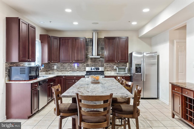 kitchen with a center island, light tile patterned floors, wall chimney range hood, and appliances with stainless steel finishes