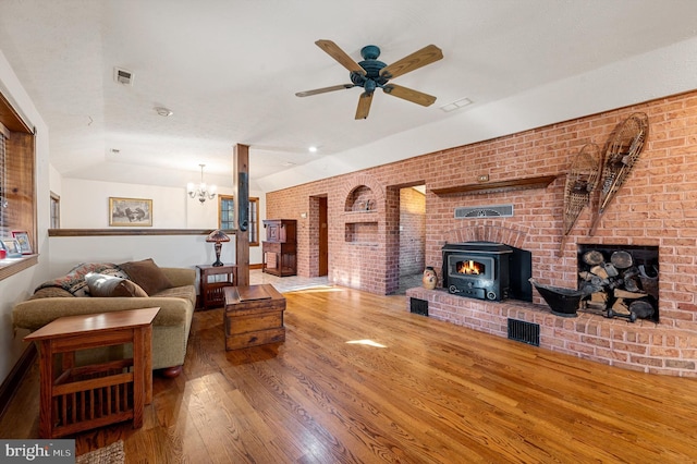 living room featuring brick wall, ceiling fan with notable chandelier, hardwood / wood-style floors, a wood stove, and lofted ceiling