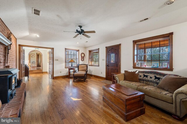 living room with a textured ceiling, ceiling fan, hardwood / wood-style flooring, a wood stove, and lofted ceiling