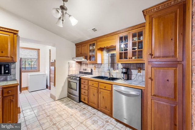 kitchen with sink, stainless steel appliances, tasteful backsplash, tile countertops, and lofted ceiling