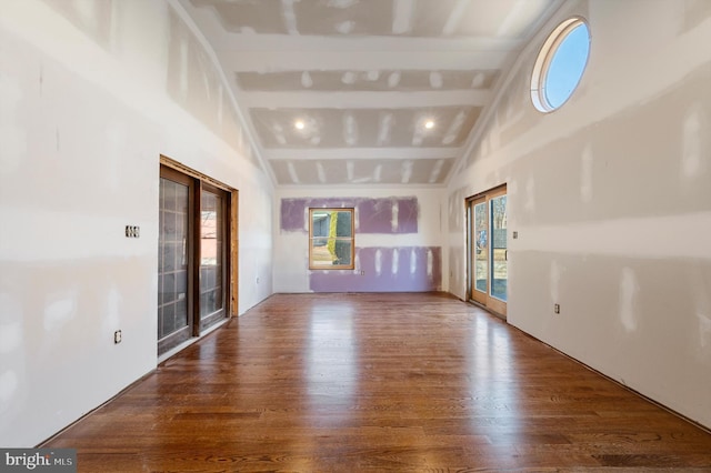 unfurnished living room featuring vaulted ceiling with beams, dark wood-type flooring, and a healthy amount of sunlight