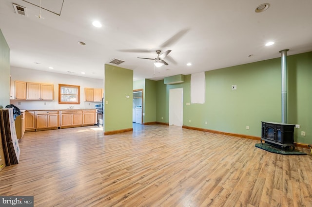 unfurnished living room featuring a wood stove, ceiling fan, sink, and light hardwood / wood-style floors