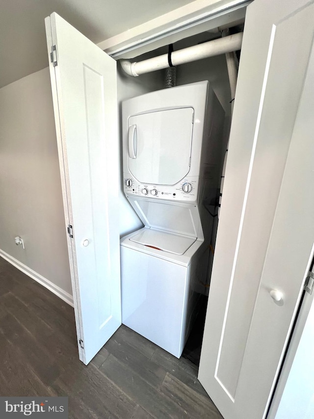 clothes washing area featuring stacked washing maching and dryer and dark wood-type flooring