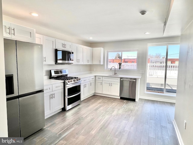 kitchen featuring appliances with stainless steel finishes, light wood-type flooring, white cabinetry, and sink