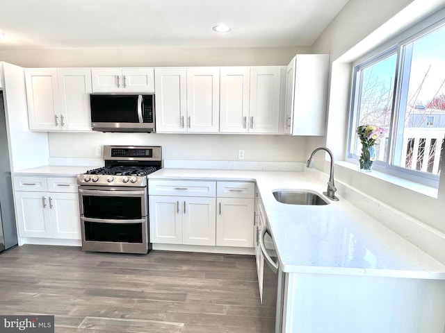 kitchen with white cabinets, appliances with stainless steel finishes, wood-type flooring, and sink