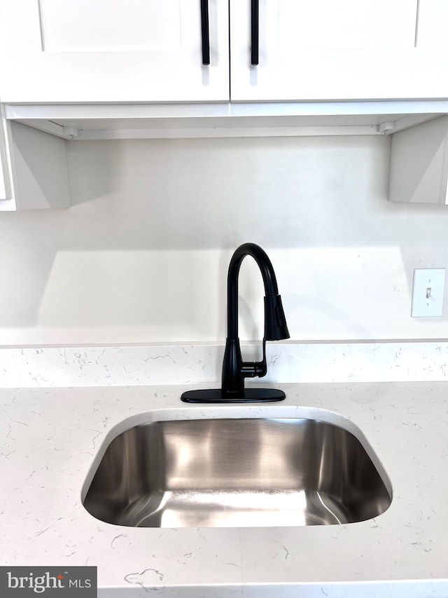 interior details featuring white cabinetry, sink, and light stone countertops