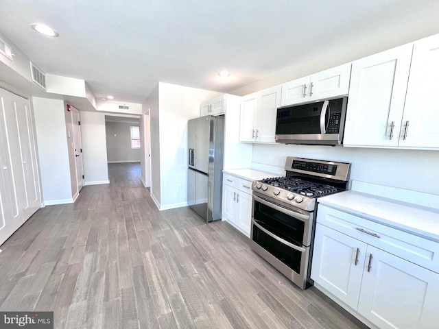 kitchen with stainless steel appliances, white cabinetry, and light hardwood / wood-style flooring