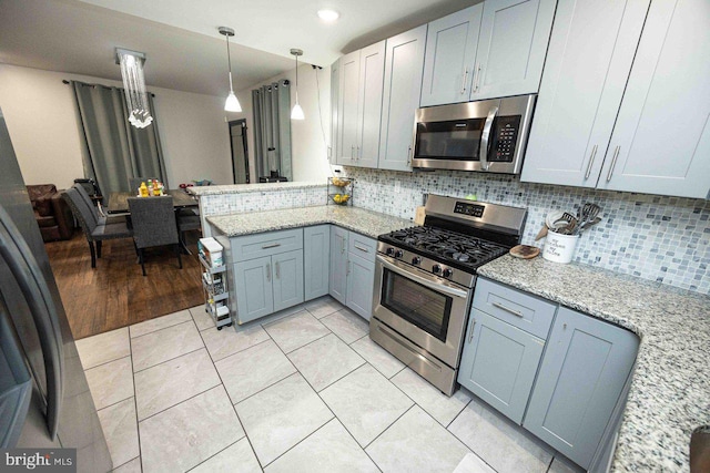 kitchen with light stone countertops, light hardwood / wood-style floors, pendant lighting, decorative backsplash, and appliances with stainless steel finishes