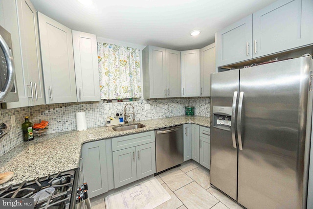 kitchen with sink, stainless steel appliances, light stone counters, backsplash, and light tile patterned floors