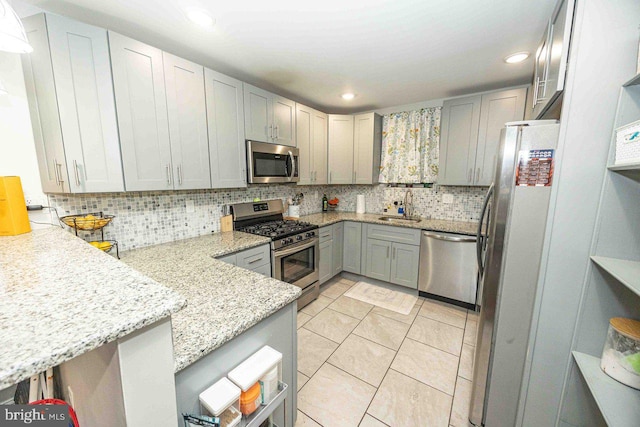 kitchen with decorative backsplash, kitchen peninsula, light stone counters, stainless steel appliances, and sink