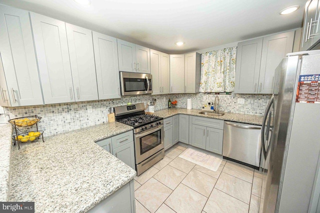 kitchen with light stone countertops, tasteful backsplash, stainless steel appliances, sink, and gray cabinets