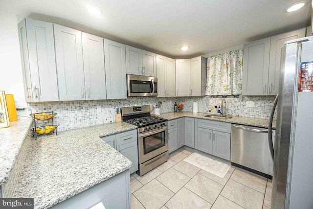 kitchen with appliances with stainless steel finishes, tasteful backsplash, light stone counters, sink, and gray cabinets