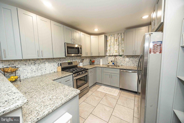 kitchen featuring gray cabinetry, sink, stainless steel appliances, tasteful backsplash, and light stone counters