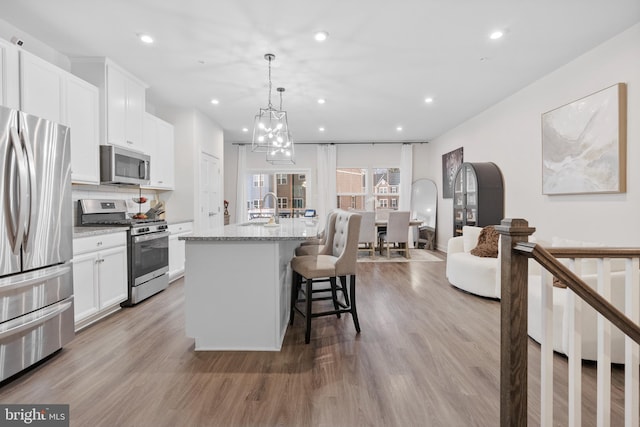 kitchen with white cabinets, light stone countertops, stainless steel appliances, and a kitchen island with sink