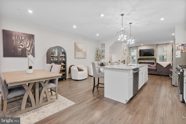 kitchen with appliances with stainless steel finishes, white cabinets, light hardwood / wood-style floors, hanging light fixtures, and an island with sink