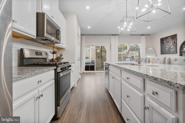 kitchen with stainless steel appliances, sink, hardwood / wood-style flooring, white cabinetry, and hanging light fixtures