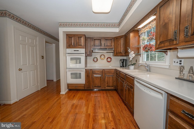 kitchen with light wood-type flooring, white appliances, and sink