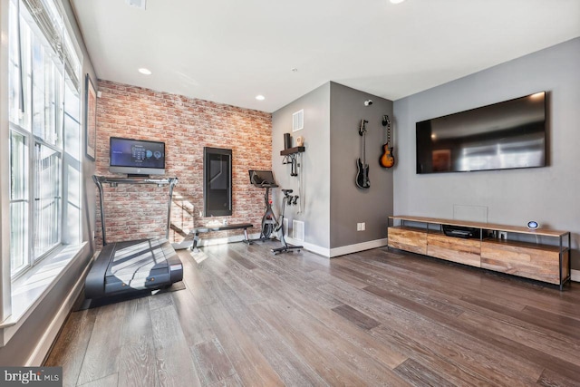 exercise room with hardwood / wood-style floors and brick wall