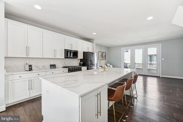 kitchen featuring dark wood-type flooring, black appliances, a kitchen breakfast bar, a center island with sink, and white cabinets