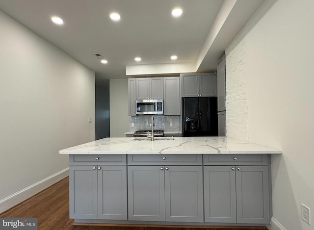 kitchen featuring light stone countertops, black fridge with ice dispenser, gray cabinets, and dark wood-type flooring