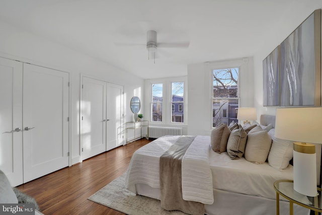 bedroom with dark hardwood / wood-style flooring, ceiling fan, radiator heating unit, and multiple closets