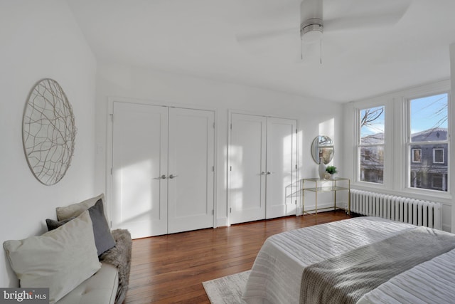 bedroom with radiator heating unit, dark wood-type flooring, ceiling fan, and multiple closets