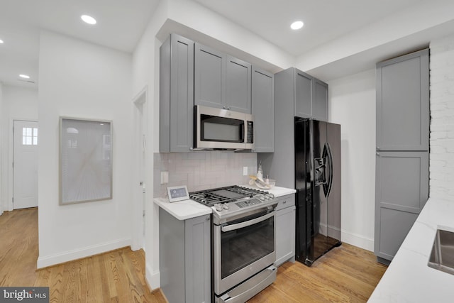 kitchen featuring gray cabinetry, decorative backsplash, stainless steel appliances, and light wood-type flooring