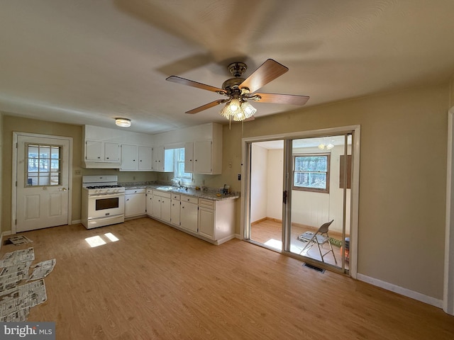 kitchen with white gas stove, a healthy amount of sunlight, light wood finished floors, and a sink