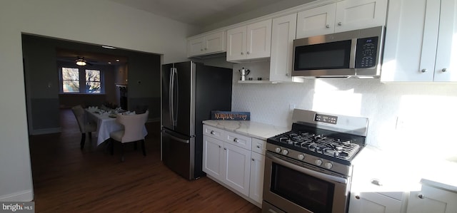 kitchen with stainless steel appliances, light stone countertops, white cabinets, dark hardwood / wood-style flooring, and decorative backsplash