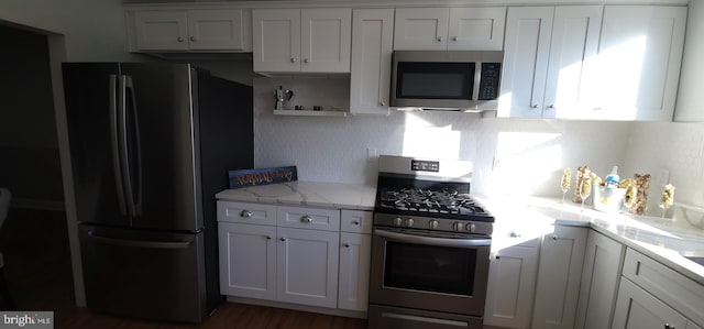 kitchen with light stone counters, appliances with stainless steel finishes, tasteful backsplash, and white cabinets