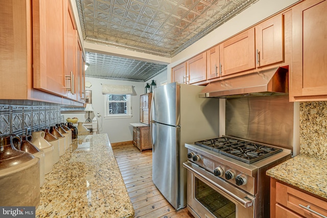 kitchen with an ornate ceiling, light stone counters, stainless steel appliances, tasteful backsplash, and under cabinet range hood