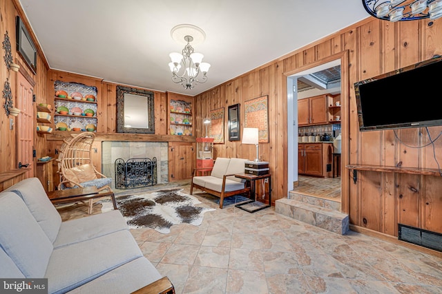 living area featuring wooden walls, visible vents, a fireplace with raised hearth, built in shelves, and a chandelier