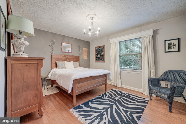 bedroom with a textured ceiling, baseboards, wood finished floors, and an inviting chandelier