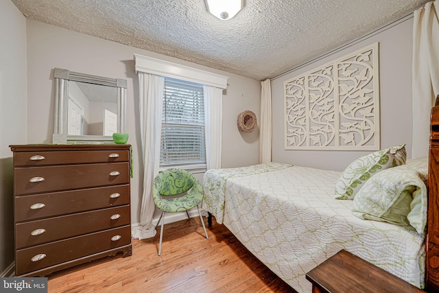 bedroom with light wood-style floors, baseboards, and a textured ceiling