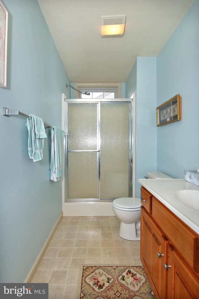 bathroom featuring tile patterned flooring, vanity, toilet, and a shower with door