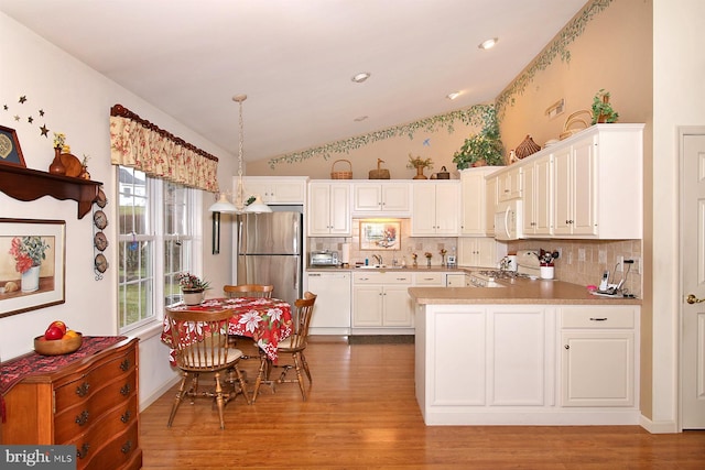 kitchen with appliances with stainless steel finishes, light wood-type flooring, vaulted ceiling, pendant lighting, and white cabinets