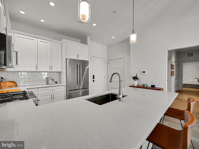 kitchen featuring sink, decorative light fixtures, decorative backsplash, appliances with stainless steel finishes, and light wood-type flooring