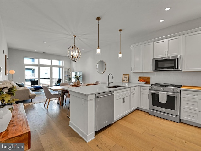 kitchen featuring white cabinetry, sink, hanging light fixtures, stainless steel appliances, and light hardwood / wood-style flooring