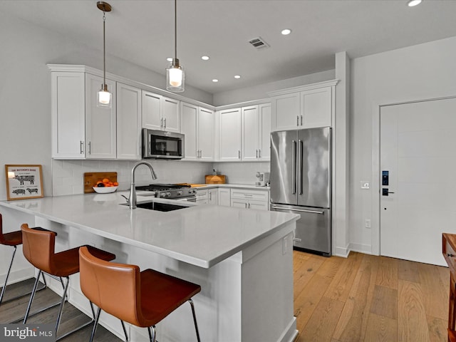 kitchen featuring kitchen peninsula, light wood-type flooring, premium appliances, white cabinetry, and hanging light fixtures