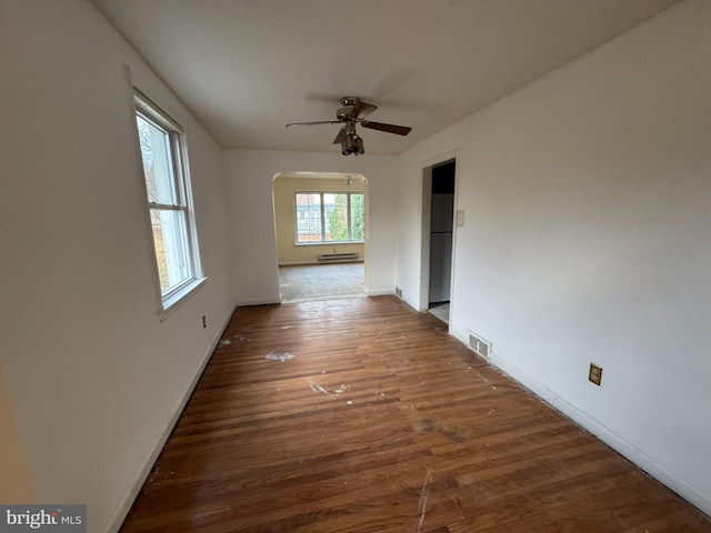 empty room featuring ceiling fan, baseboard heating, and dark wood-type flooring