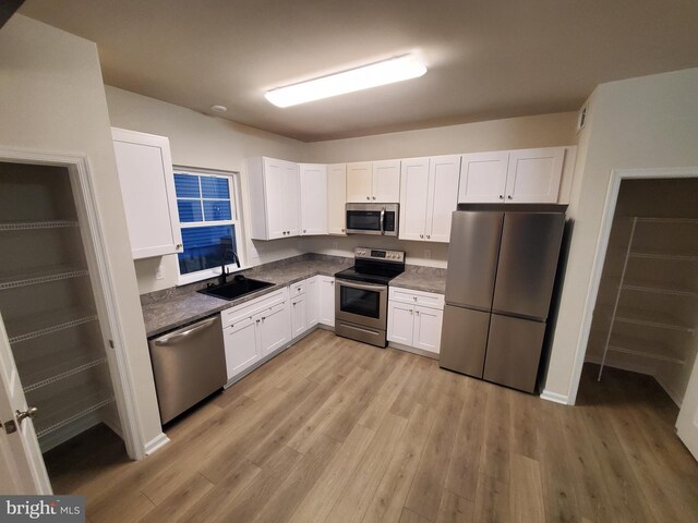 kitchen with sink, white cabinets, light hardwood / wood-style floors, and appliances with stainless steel finishes