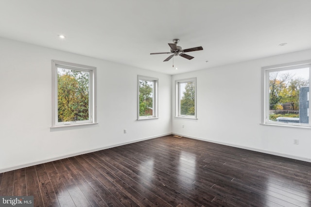 empty room featuring a wealth of natural light, ceiling fan, and dark wood-type flooring