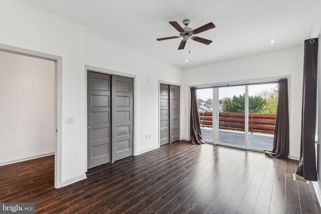 unfurnished bedroom featuring access to outside, dark hardwood / wood-style floors, ceiling fan, and multiple closets